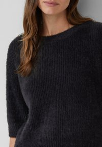 Czarny dzianinowy sweter z prążkowaną teksturą, z rękawami o długości trzech ćwiartek i szerokim dekoltem. Miękki, puszysty materiał. Brak widocznych elementów metalowych.