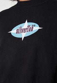 Felpa nera in cotone con logo ovale blu, una stella bianca e la scritta "silverTab®" in rosa. Texture morbida e design semplice.
