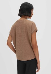 Top corto marrone a maniche corte con design a maglia testurizzata, colletto rotondo e vestibilità ampia, indossato con pantaloni neri, visto da dietro.