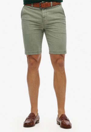 Shorts en denim vert clair avec une coupe droite, passants de ceinture et poches latérales. Associés à des mocassins en cuir marron. Tissu texturé.