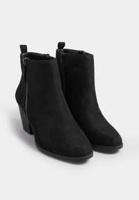 Par de botines de ante negro con cremalleras laterales y tacones de bloque sobre un fondo blanco.