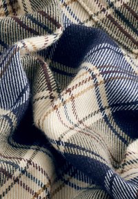 Țesătură din amestec de lână cu un model în carouri crem, bleumarin și burgund. Textură moale cu țesătură fină vizibilă și un design predominant în carouri.