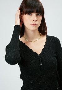 Schwarzer, gerippter Pullover mit einem gewellten Ausschnitt, drei Knöpfen und langen Ärmeln mit strukturiertem Finish und subtiler Shimmer.