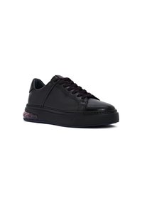 Zapatilla de cuero negra de corte bajo con cordones negros, suela gruesa y detalle de talón acolchado translúcido, vista desde un ángulo frontal bajo.