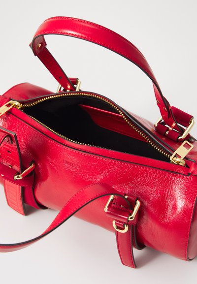 Sac à main en cuir rouge avec quincaillerie dorée, fermeture éclair, anses doubles et accents texturés. L'intérieur est doublé de matériau noir.