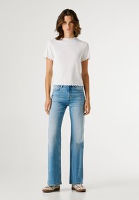 Λευκό ριμπ μπλουζάκι με κυματιστά τελειώματα, συνδυασμένο με ανοιχτό μπλε φαρδιά τζιν. Το υπόδημα έχει λουλουδάτο σχέδιο. Ζωηρή, καθαρή εμφάνιση.