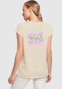 Beige short-sleeved t-shirt with roll sleeves, featuring colorful text on the back that reads "BLOOM LIVE SIMPLY WIDELY" in pink and green.