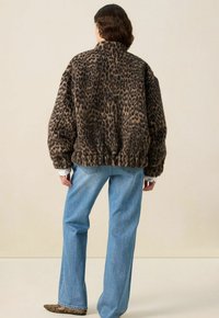 Veste en fausse fourrure au motif léopard avec une coupe oversize, col haut, ourlet élastique et manches longues ; associée à un jean droit bleu clair.