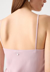 Lyserød ærmeløs top med tynde stropper, der har en glat overflade og en lille metalknapdetalje bagpå. Enkle og elegante design.