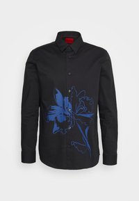 Chemise noire à manches longues, boutonnée, col pointu et grand motif floral bleu sur le côté avant gauche.