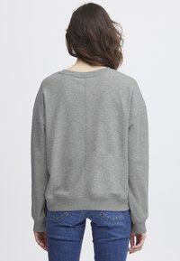 Sudadera gris, de gran tamaño, con cuello redondo, mangas largas y puños acanalados. Fabricada en una suave mezcla de algodón con una textura lisa.
