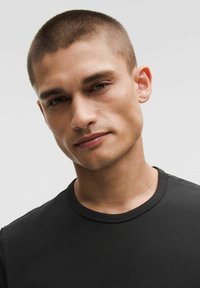 Svart t-shirt med rund halsringning och korta ärmar. Slät textur, åtsittande design. Modellen har kort, ljust hår och är centrerad i ramen.