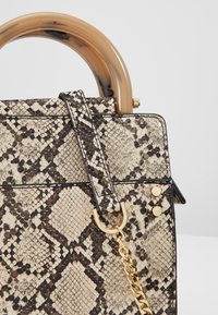 Gros plan d’un sac à main en cuir de serpent beige et noir avec une poignée ronde en écaille de tortue et un détail de chaîne dorée.