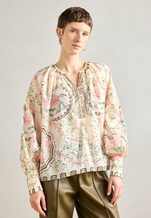 Blusa floreale leggera in crema con motivi rosa e verdi. Presenta un scollo a V, maniche arricciate e ricami intricati lungo l'orlo.