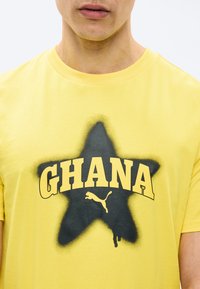 Άνδρας που φοράει κίτρινη μπλούζα με μαύρο αστέρι και κείμενο "GHANA" πάνω από το λογότυπο Puma στο στήθος.