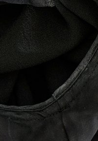 Gros plan d'un tissu noir avec des coutures visibles et une doublure intérieure texturée, montrant les plis et les coutures d'un vêtement ou accessoire.