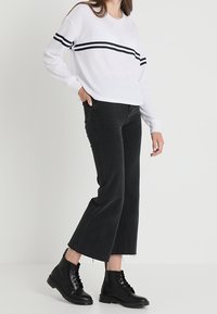 Vitt ribbat tröja med svarta horisontella ränder, matchad med högmidjade svarta jeans och svarta snörstövlar, som visar en avslappnad passform.