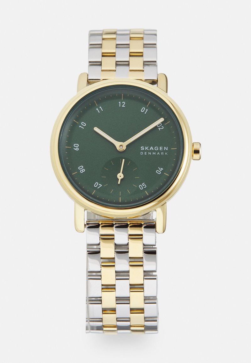 Rund klokke med en grøn urskive, gyldne visere og et subur. Sølv- og guldfarvet rustfrit stålarmbånd med led. Minimalistisk design med klare time markeringer.