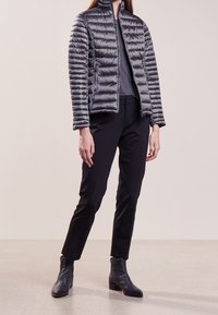 Grau gepolsterte Jacke mit horizontalen Streifen, hohem Kragen und durchgehendem Reißverschluss. Kombiniert mit schwarzen, taillierten Hosen und Stiefeletten.