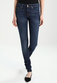 Jeans skinny de color azul oscuro con detalles de costura clara, bolsillos frontales y un diseño ajustado. Hechos de tela de mezclilla.