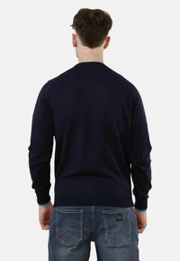 Maglione blu navy a maglia con maniche lunghe e scollo rotondo, indossato con jeans blu caratterizzati da un sottile design della tasca posteriore.