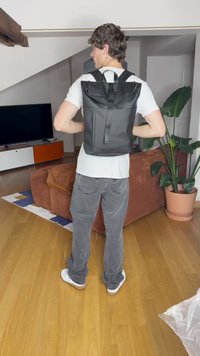 Czarna skórzana plecak o designie z rolowanym wiekiem, z regulowanymi paskami, przednią kieszenią na zamek błyskawiczny i matowym wykończeniem, eksponowany na neutralnym tle wnętrza.