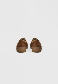 Hnědé semišové neformální boty s kulatým tvarem, plochými gumovými podrážkami a dekorativním šitím na zadní straně s malými poutky.