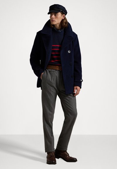 Navy wool peacoat with large collar, paired with a navy and red striped sweater, gray trousers, and brown lace-up shoes.