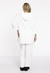 Weißer Kapuzenpullover mit lockerer Passform und strukturiertem Material, kombiniert mit passenden weißen Hosen. Beide Teile haben ein entspanntes, bequemes Design.