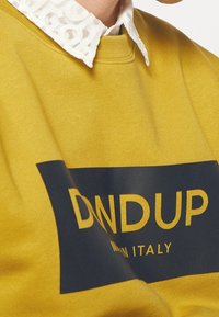 Żółta bluza z kapturem z granatowym prostokątnym logo z napisem "DNDUP" oraz tekstem "MADE IN ITALY". Wykonana z bawełny, z prążkowanym dekoltem.