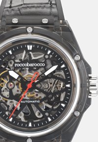 Transparente Uhr mit schwarzem Lederarmband, Skelettzifferblatt, das komplizierte Zahnräder zeigt, weißen und roten Zeigern sowie silbernen Akzenten.