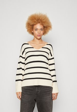 Suéter de rayas blancas y negras de manga larga con escote en V y corte relajado, combinado con pantalones de mezclilla gris. Textura suave y estilo casual.
