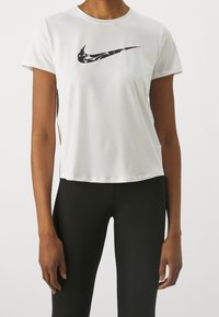 Bílý sportovní tričko s krátkými rukávy, se slavným černým logem Nike na přední straně. Vyrobeno z hladkého, lehkého materiálu.