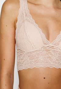 Lace bralette in soft pink with a deep V-neck, floral patterns, scalloped edges, and wide straps for added support.