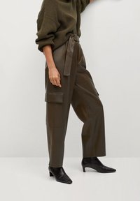 Zielone oliwkowe spodnie cargo z sztucznej skóry, z wysokim stanem, wiązaniem z przodu i dużymi bocznymi kieszeniami. Noszone z czarnymi, spiczastymi botkami za kostkę.