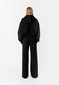Sudadera negra de gran tamaño con capucha, combinada con pantalones anchos negros. Elaborada en una tela suave, presenta un diseño minimalista y sin logotipos visibles.