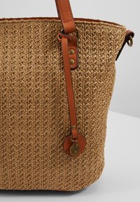 Geweven strooien totebag in beige met een soepele bruine leren band en een ronde leren label met metalen accent.
