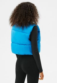 Blå puffväst med quiltat mönster, hög krage och ärmlös design. Bärs över en svart långärmad topp och matchas med svarta byxor.