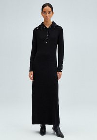 Abito nero a coste con maniche lunghe, colletto, chiusura con bottoni e bottoni decorativi sui polsini. Design lungo fino al pavimento.