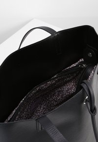 Czarna torba na ramię ze skóry z podwójnymi uchwytami, wyposażona w kieszeń na zamek i podszewkę w kwiatowy wzór. Gładka faktura, minimalistyczne elementy metalowe.