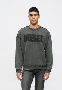 Sweatshirt cinza escuro com gola redonda, apresentando um logótipo texturizado "DIESEL FOR SUCCESSFUL LIVING" na frente. Bordas desgastadas visíveis.