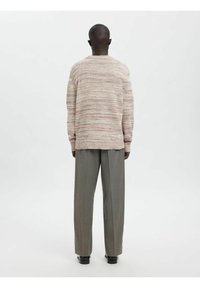 Gestrickter Pullover mit einem strukturierten, mehrfarbigen Muster in sanften Tönen, kombiniert mit hellgrauen, maßgeschneiderten Hosen und schwarzen Schuhen.