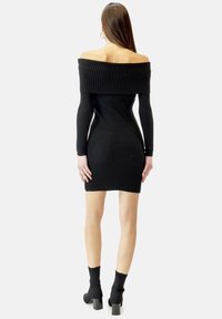 Schwarz, schulterfreies, geripptes Strickkleid mit langen Ärmeln, enganliegender Silhouette und mittlerer Oberschenkel-Länge; kombiniert mit schwarzen, hochhackigen Ankle-Boots.