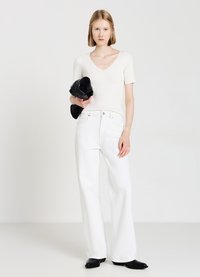 Jeans bianchi a vita alta e a gamba larga, top corto a maniche corte color avorio a coste con scollatura a V, e borsa a tracolla nera. Il modello indossa scarpe con tacco nere.