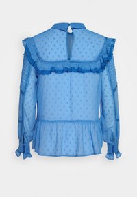 Vaaleansininen, puoliksi läpikuultava pusero, jossa on tekstuurilla varustettuja pisaroita, röyhelökaulus ja kerroksittain laskostettu helma. Pitkissä hihoissa on napilla varustetut hihansuut.