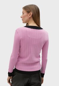 Ljusrosa ribbad tröja med svart krage och mudd. Har en figurnära design och långa ärmar, som visar vertikalt randig textur.