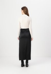 Svart satengmaxikjole med en tettsittende midje, splitt detalj bak, kombinert med en lysfarget langermet topp. Glatt tekstur.