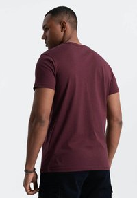 Burgunderfarbendes Crewneck-T-Shirt mit kurzen Ärmeln, aus weichem Stoff, figurbetontem Design und glatter Textur, von hinten präsentiert.