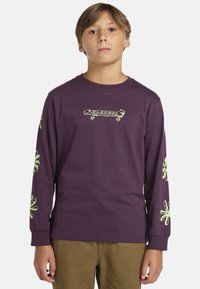 Långärmad lila t-shirt i bomull, med en skateboardgrafik i grönt och blommönster på ärmarna. Avslappnad passform, rundad hals.