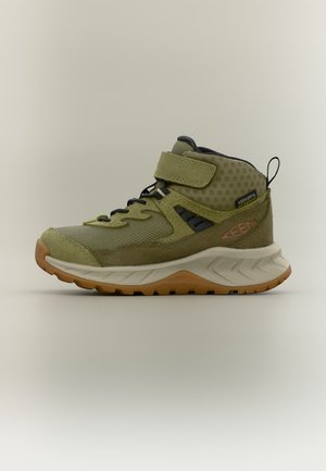 Zapatilla deportiva alta de color verde oliva con cordones negros, cierre de velcro, suela texturizada y lengüeta para tirar, diseñada para actividades al aire libre.
